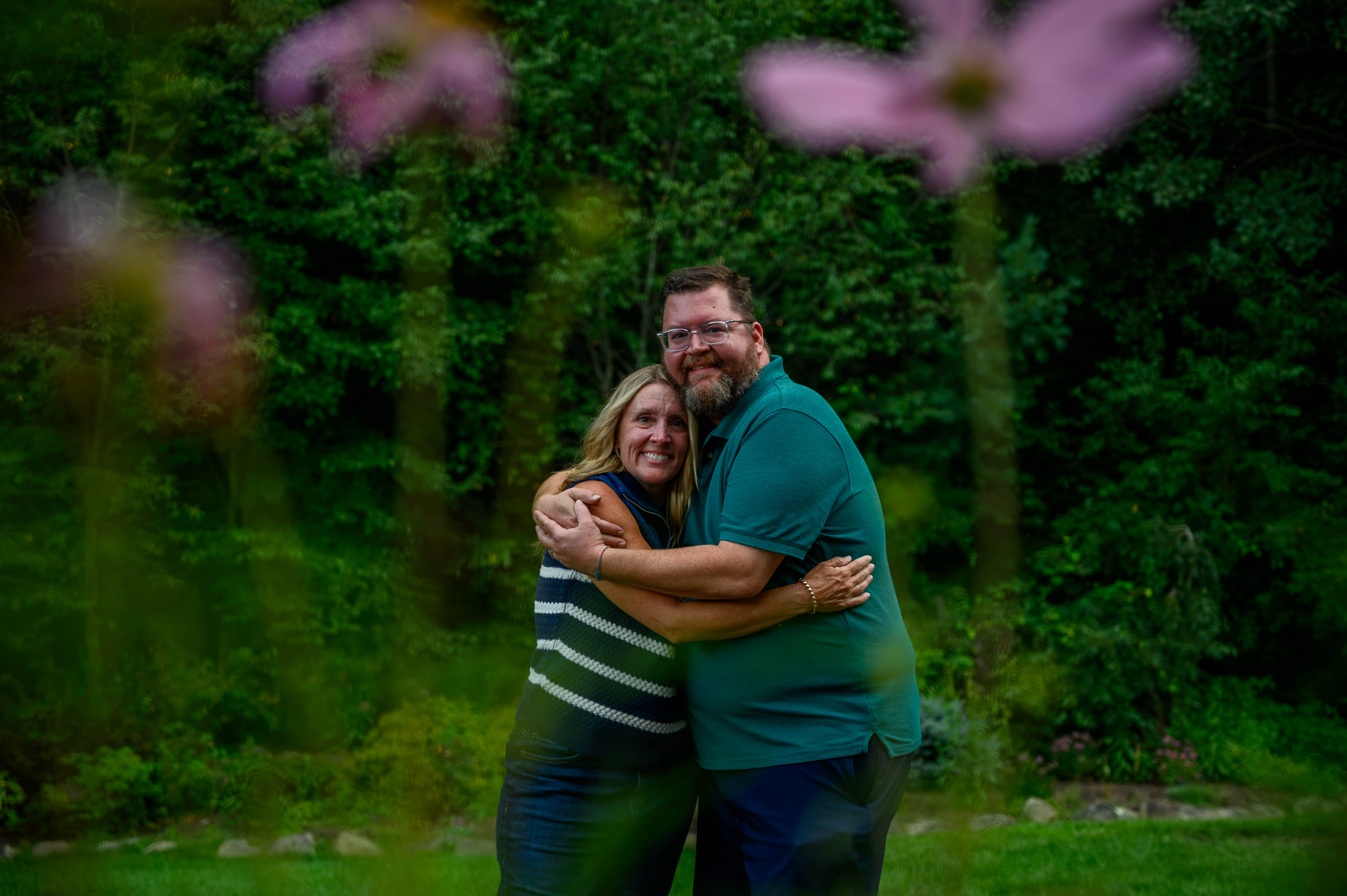Two adult siblings hugging eachother framed between flowers.